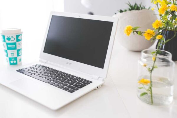 Acer chromebook on white desk with flower in vase beside it.jpg