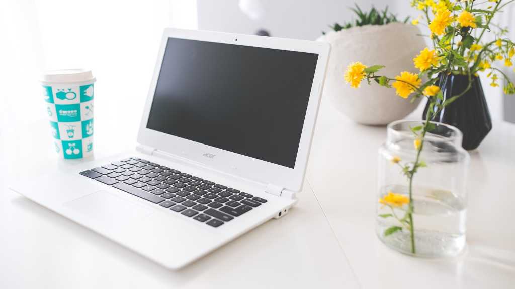Acer chromebook on white desk with flower in vase beside it.jpg
